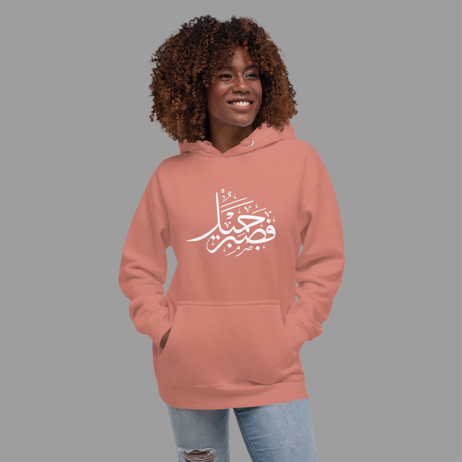 Person wearing a pink hoodie with Arabic text on a gray background